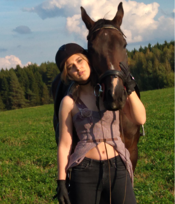 Фотография девушки рядом с тёмно-гнедой лошадью во время фотосессии в поле.